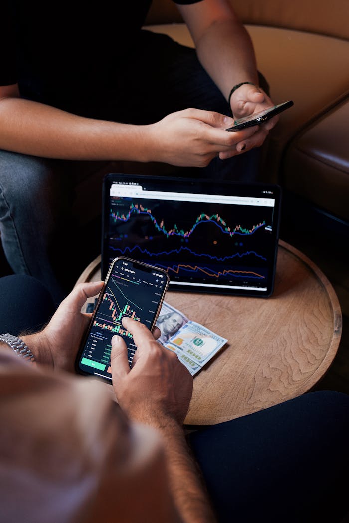 Services Two people using smartphone and tablet for trading stocks indoors.